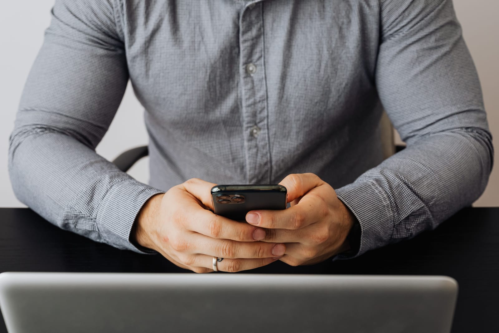 Person typing a message on a smartphone at a desk beside a laptop