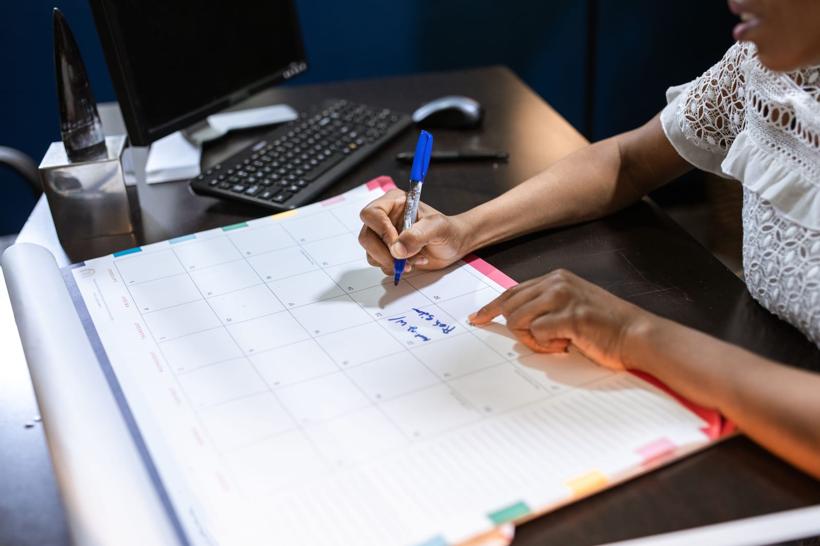 Wall calendar with marked days beside a desk and laptop